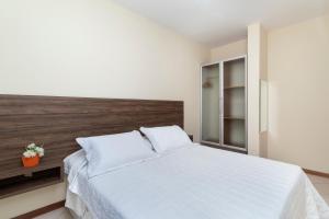 sypialnia z białym łóżkiem z drewnianym zagłówkiem w obiekcie Acapulco - Apartamentos em Bombinhas w mieście Bombinhas