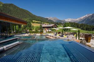 ein Pool mit Stühlen und ein Haus und Berge in der Unterkunft Hotel Plunhof in Ridnaun