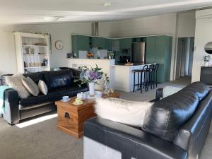 a living room with black leather couches and a kitchen at Mariri Heights Tasman in Upper Moutere
