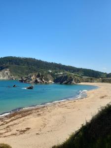 Pension Bajamar في Ladrido: شاطئ فيه ماء ازرق وصخور من بعيد
