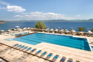 a swimming pool with chairs and umbrellas next to the water at Ramada Loutraki Poseidon Resort in Loutraki