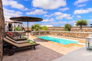 una piscina con due lettini e un ombrellone di El Caserío de Güime Villa con Piscina Climatizada a San Bartolomé