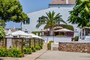 a white building with a fence and umbrellas at Hotel Rural Sant Joan de Binissaida in Es Castell