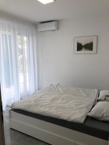 a white bedroom with a bed and a window at Rezeda Apartman in Fonyód