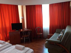 a hotel room with red curtains and a couch and a tv at Pensiunea Sydney in Timişoara