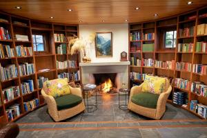 a library with two chairs and a fireplace at Cabot Lodge - Fiordland National Park in Manapouri