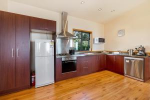 a kitchen with a white refrigerator and wooden cabinets at Moeraki with private walkway to Onetangi Beach by Waiheke Unlimited in Onetangi