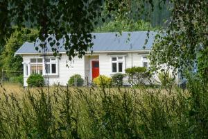 une maison blanche avec une porte rouge dans un champ dans l'établissement Orinoco Country Retreat, à Ngatimoti