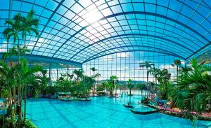 a large indoor pool with palm trees and a glass ceiling at Hotel Kick in Rauenberg