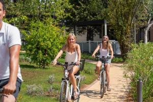 two women riding bikes down a path in a park at Mobile Homes Camping Santa Marina, Lanterna in Poreč
