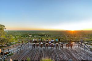people sitting at tables on a viewing deck at sunset at Gondwana Damara Mopane Lodge in Mopane Pos