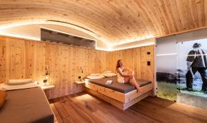 a woman sitting on a bed in a room with wooden walls at Bar Garni Reischnhitt des Eschgfeller Christoph in Sarntal
