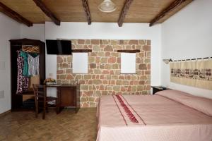 a bedroom with a bed and a desk and a stone wall at Hotel Goloritzé in Baunei