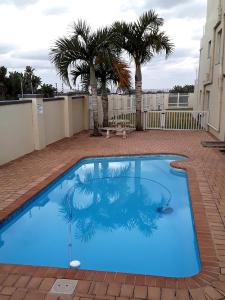 a blue swimming pool with palm trees in the background at 12 Uvongo Breeze in Uvongo Beach