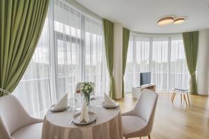 - une salle à manger avec une table, des chaises et de grandes fenêtres dans l'établissement Luxury Apartments, à Druskininkai