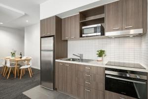 cocina con nevera de acero inoxidable y mesa en Quest Caroline Springs, en Caroline Springs