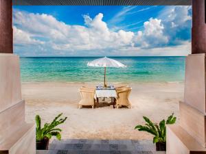 a table on the beach with an umbrella and chairs at Montien House - SHA Plus in Chaweng