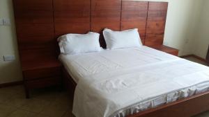 ein großes Bett mit weißer Bettwäsche und einem Kopfteil aus Holz in der Unterkunft Hotel Dot Com Entebbe in Entebbe