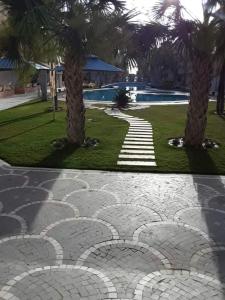een stenen loopbrug met palmbomen en een zwembad bij Dunes ressort chott Meriem in Sousse