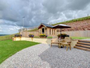 a house with an umbrella and a table and benches at Holiday Home Crow by Interhome in Witheridge