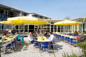 eine Gruppe von Menschen sitzt an Tischen mit gelben Sonnenschirmen in der Unterkunft GenoHotel Karlsruhe in Karlsruhe