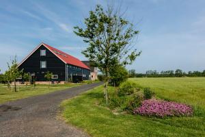 a black barn with a red roof next to a field at Hofwestdijk in Vrouwenpolder