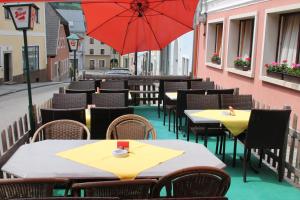 um pátio com mesas e cadeiras e um guarda-sol vermelho em Gasthof-Cafe-Risano em Haslach an der Mühl