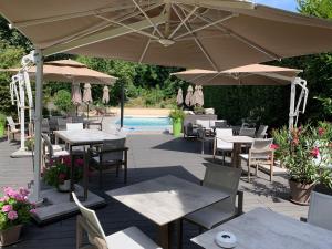 a patio with tables and umbrellas and a pool at Logis Hotel Le Petit Casset in La Boisse
