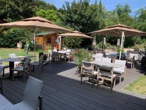 una terraza de madera con mesas, sillas y sombrillas en Logis Hotel Le Petit Casset, en La Boisse