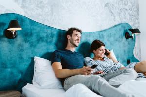 Een man en vrouw die op een bed naar hun mobieltjes zitten te kijken. bij Hotel Rainers21 in Brunn am Gebirge