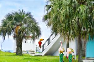 two flamingos standing next to a house with palm trees at Nagasaki Chapel Coconuts Hotel ＆Resort in Isahaya