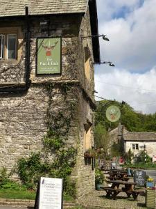 un panneau sur le côté d'un bâtiment avec une table de pique-nique dans l'établissement The Buck Inn, Malham, à Malham