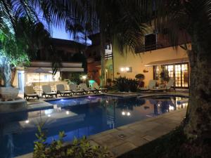 a swimming pool with chairs and a resort at night at Hotel Costa Balena, Conforto e Piscina aquecida e coberta a 100m da Praia da Enseada in Guarujá