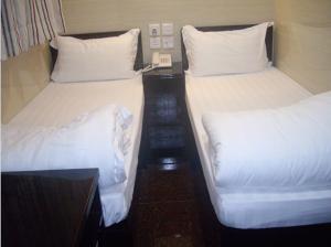 2 łóżka w małym pokoju z białą pościelą i poduszkami w obiekcie Simplex Guest House w Hongkongu
