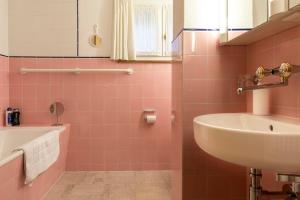 La salle de bains rose est pourvue d'un lavabo et d'une baignoire. dans l'établissement Casa Vesta Magnifica Wildi, à Brigels