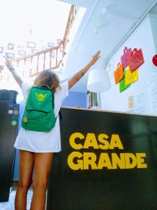 Una donna con uno zaino verde accanto a un cartello di Casa Grande Surf Hostel a El Médano