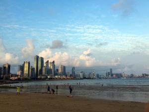 um grupo de pessoas numa praia com uma cidade ao fundo em Qingdao Elegant Central Apartment em Qingdao