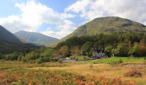 a house in a field with mountains in the background at Birch Chalet in Ballachulish