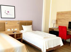 Habitación con 2 camas, escritorio y silla roja. en Turm Hotel Hanau, en Hanau am Main