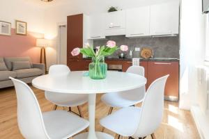 a white dining room table with white chairs and pink flowers at ALTIDO Bright Apartment for 4 next to City Life in Milan
