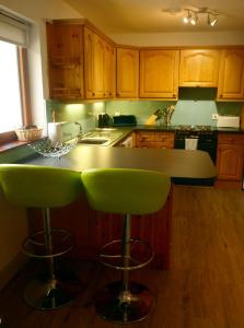 una cocina con armarios de madera y taburetes de bar verde en Holly Tree Cottage, en Glencoe