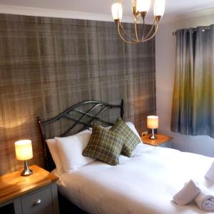 a bedroom with a bed with two lamps and a chandelier at Holly Tree Cottage in Glencoe
