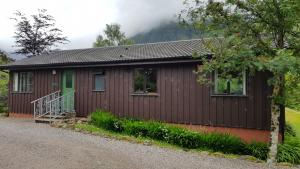 a small cabin with a green door and a gravel driveway at Oak Tree Lodge in Ballachulish
