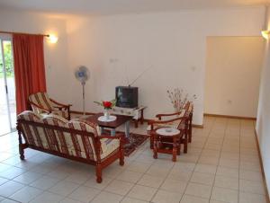 a living room with chairs and a table and a tv at Rowsvilla Guest House in Beau Vallon