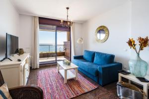 Sur Suites Buena Vista في فوينخيرولا: غرفة معيشة مع أريكة زرقاء وإطلالة على المحيط