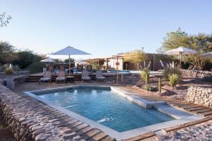 uma piscina com cadeiras, uma mesa e um guarda-sol em Hotel Cumbres San Pedro de Atacama em San Pedro de Atacama