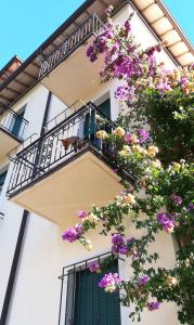 ein weißes Gebäude mit einem Balkon mit lila Blumen in der Unterkunft Ostello delle cartiere in Toscolano-Maderno