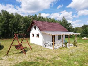 a small white shed with a swing and a playground at Kaszubska Dolina Pięciu Stawów in Wiele