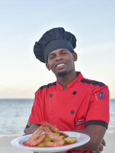 a man in a chef outfit holding a plate of food at Ifa Beach Resort in Jambiani