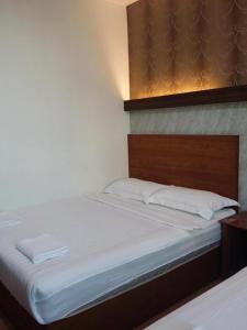 a bed with white sheets and a wooden headboard at Maxi Inn in Bintulu